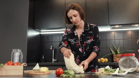 Woman kneading dough on wooden table with flour while working in kitchen