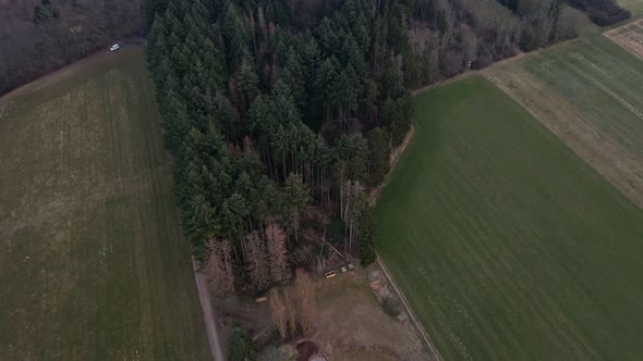 European farm land between green fields and mixed forests. Aerial reveal shot