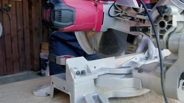 Carpenter in Protective Gloves Cuts Off Wooden Oak Bar on Mitre Saw Close-up