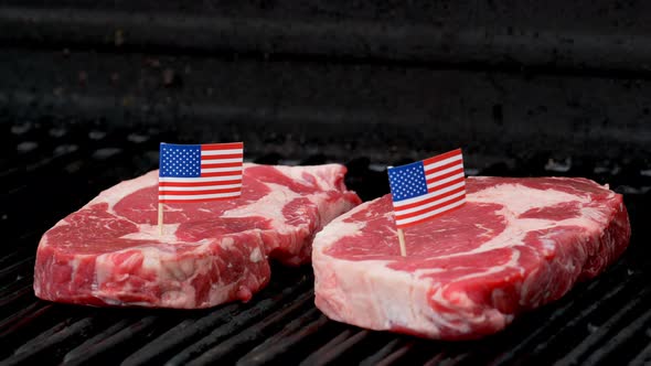 Two juicy rib-eye steaks sitting on the grill and cooking with two tiny American flags tooth picked