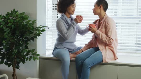 Lesbian couple having coffee sitting on window sill