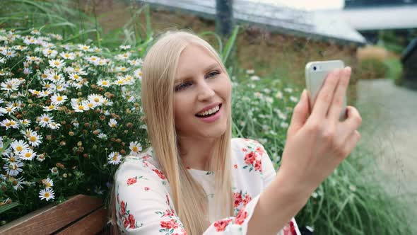 Lovely Young Lady Using Smartphone To Make Video Call While Sitting on Bench on Living Roof of Huge