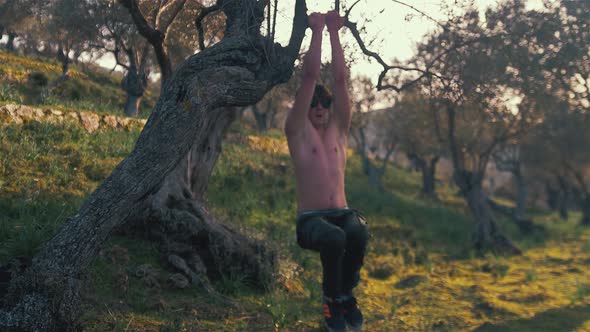 Young strong lean fit man doing hanging L-sit raises within nature using tree