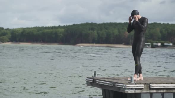 Professional Swimmer Triathlete in Wetsuit for Swims Walks Along the Pier and Prepares to Jump Into
