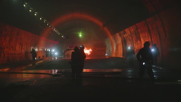 Firefighters inside a dark tunnel with emergency lights in the background