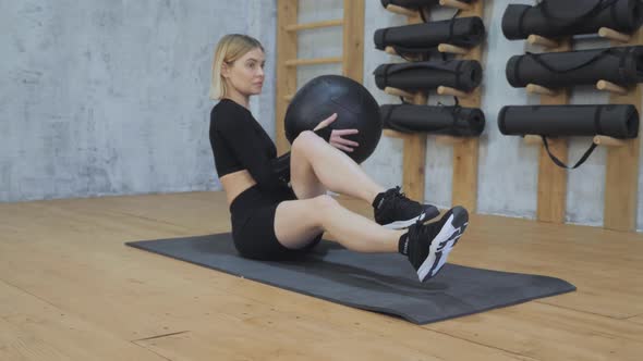 A Young Athletic Blonde Woman Does A Belly Press Exercise With A Sports Ball in a Black Top