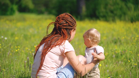 Mom with a child are sitting in a clearing or park. Parenting Maternity Joy Family Concept.