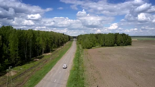 White Car Drives on Gray Road Near Old Power Lines Aerial