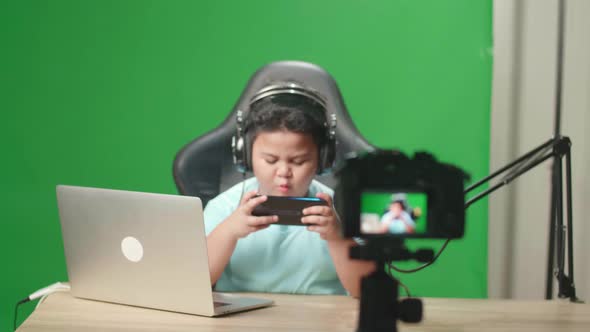 Camera And Asian Little Boy Playing Video Game With Mobile Phone And Say Something On Green Screen alt