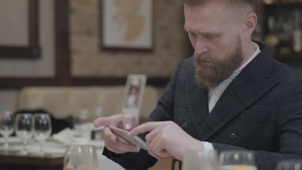 Confident Blond Bearded Man in Stylish Jacket Taking a Photo of His Food with His Cellphone Sitting