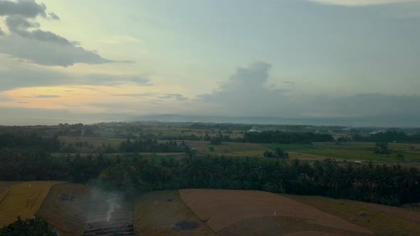 Beautiful sunset aerial over rice crop fields in rural Bali with smoke plumes coming from burning st