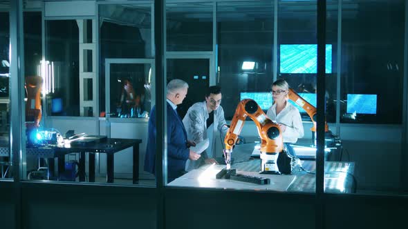 Three Engineers Discussing Industrial Robot Capabilities at Laboratory