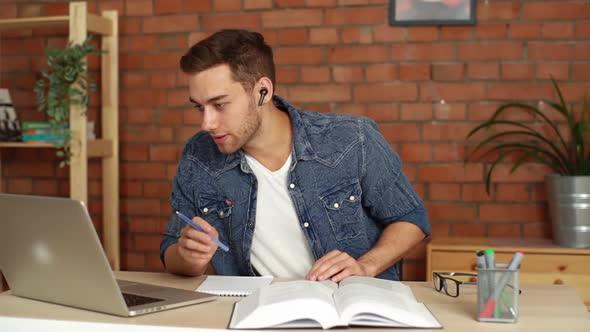 Front View of Focused Guy Student Wearing Wireless Headset Elearning By Web Cam and Making Notes