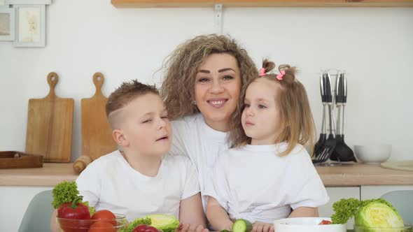 A Boy and a Girl with Their Mother are Sitting at a Table in a Bright Kitchen