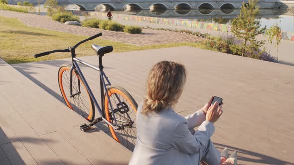 Businesswoman with Bike Using Smartphone at Waterfront