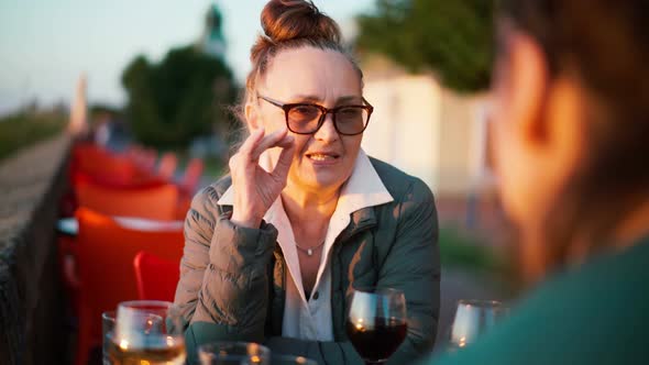 Mature Woman in Glasses Sitting in a Cafe with Her Daughter and Drinking Wine