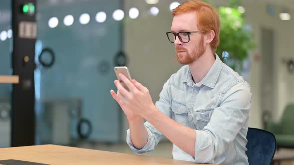 Attractive Redhead Man Having Success on Smartphone in Office 