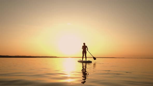 Siluet of Woman Standing Firmly on Inflatable SUP Board and Paddling Through Shining Water Surface