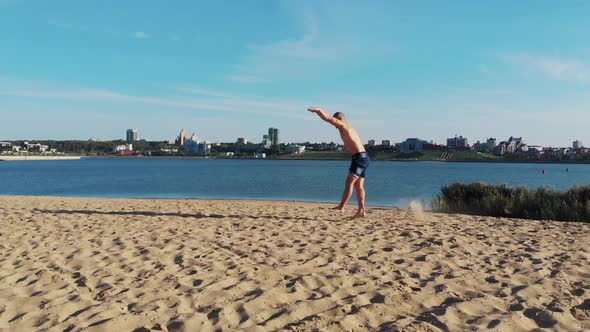 Young Man Running Up and Starts Doing a Series of Flips on the River Coast