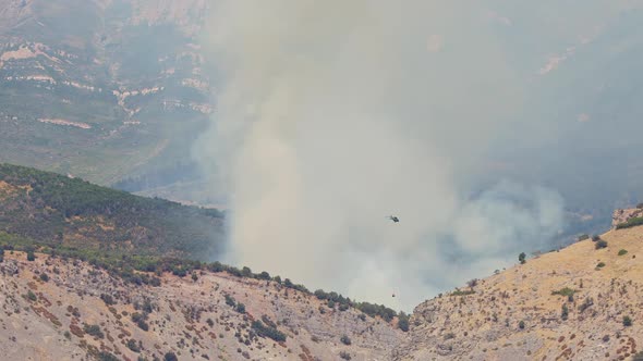 Wildfire burning as helicopter with bucket drops water to control it