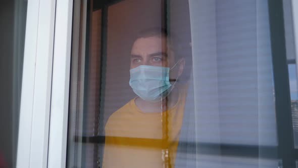 COVID-19 Pandemic Coronavirus. Quarantine Man in Medical Mask on Face Looking Through the Window