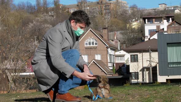 Man Wears Mask and Holds Smartphone Near Playing Small Dog