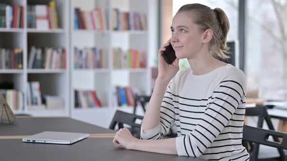 Cheerful Young Woman Talking on Smartphone in Library 