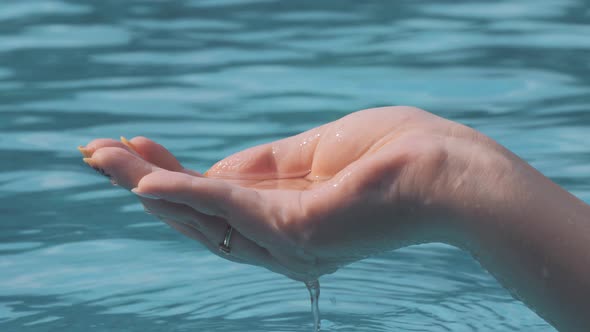 Closeup Shot of Female Hand Playing with Water Catching It with Fingers and Pouring Into a Pool on