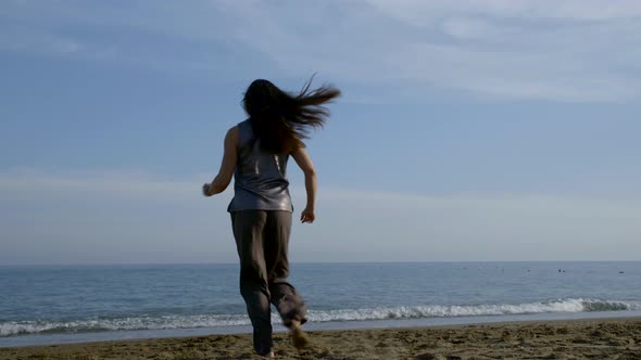 Dark-haired Woman in Wide Pants Barefoot Jumping and Spinning on a Sandy Beach Near the Sea.