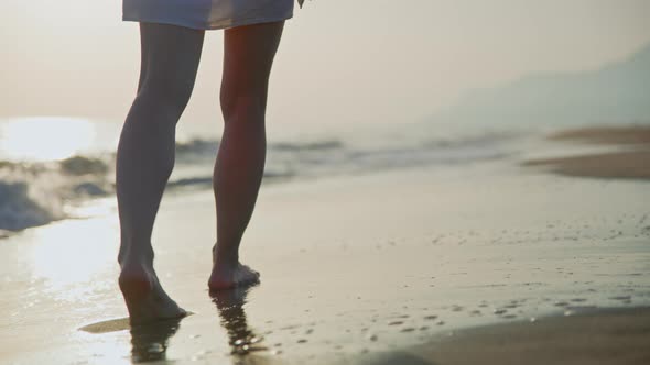 Young barefoot girl walking along the seashore in summer