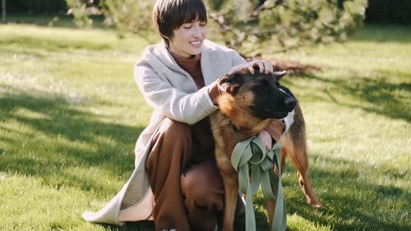 Stylish Young Woman Playing with Dog in the Garden at Sunset Time