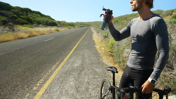 Triathlete man drinking water in the countryside road