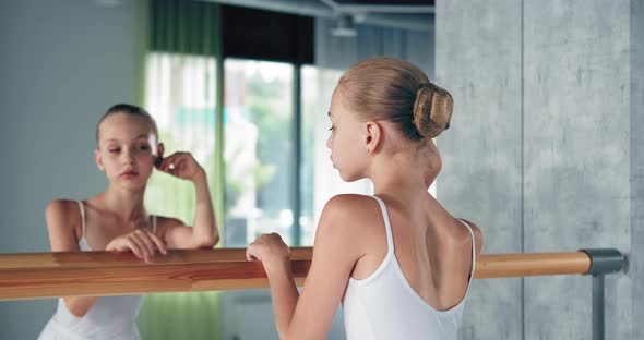 Girl with Bun Looks Into Large Mirror Leaning on Barre