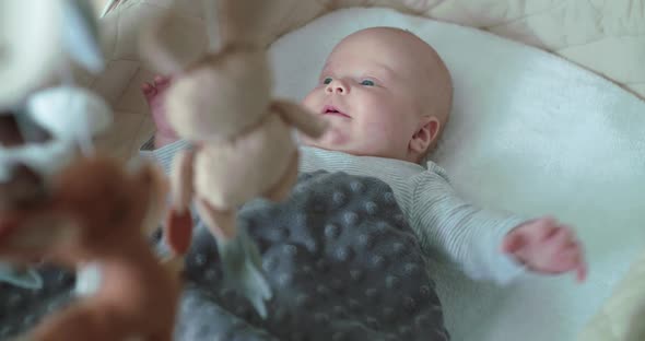 Happy Baby Boy Lying in Bed with Moving Toys Looking Around and Rejoicing