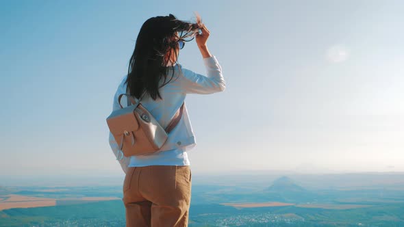 Young Woman with Backpack Standing on Cliff and Looking To a Sky