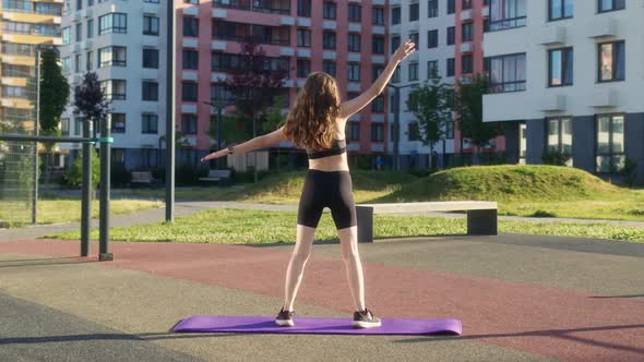 Young Woman in Black Sportswear is Stretching on Sports Ground and Bending to Left and Right