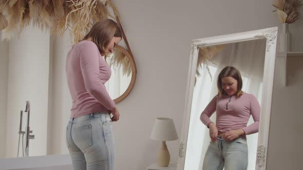 Unhappy Pretty Female Trying to Squeeze Into Old Tight Pair of Jeans in Front of Mirror