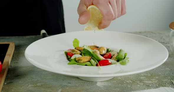 Close Up View of a Man Hand Chef Squeezing Fresh Lemon Making Fresh Mussel Salad