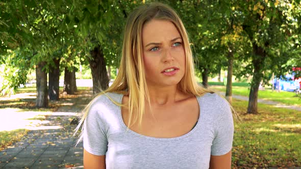 Young Pretty Blond Woman Is Angry - Park with Trees in Background