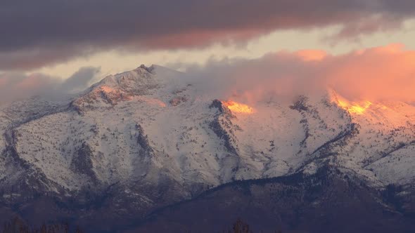 Panning view of snow covered mountain peaks lit up at sunrise