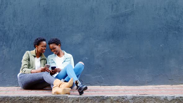 Twin sisters using mobile phone on a sidewalk in the city 4k