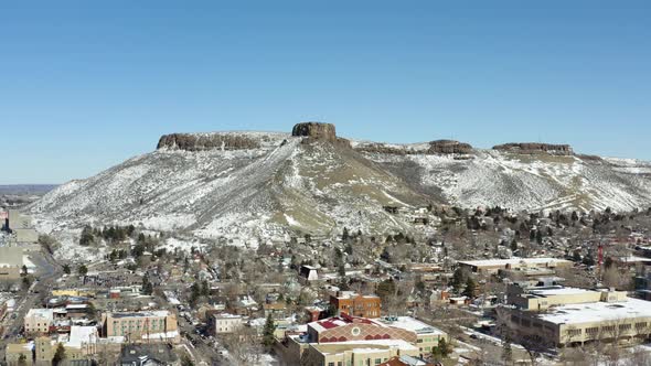 An aerial crane up shot of a town overlooking a snowy mountain during the winter.