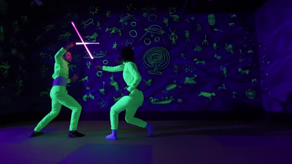 Fencing Young Couple's Date Having Fun in a Neon Amusement Park Guy and a Female are Fighting with