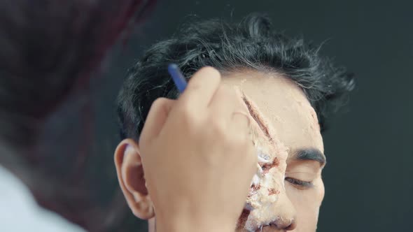 Make up artist coloring prosthetic insert on man's face and making a Halloween mask