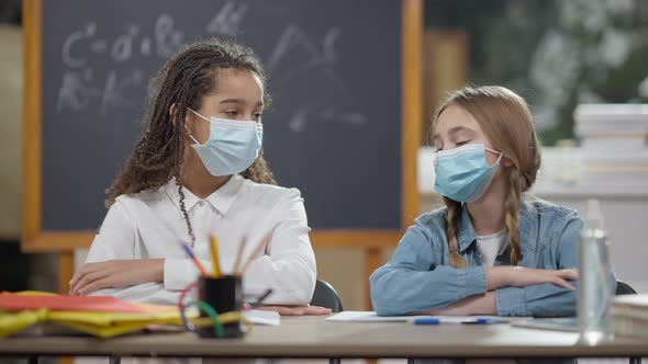 Caucasian and African American Junior High Students in Coronavirus Face Masks Sitting at Desk