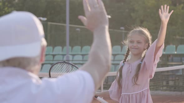 Cute Little Smiling Happy Girl with a Tennis Racket in Her Hands Standing on the Tennis Court