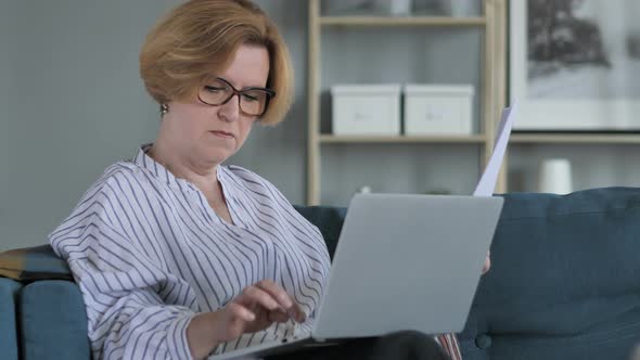 Pensive Old Woman Doing Paperwork and using Laptop