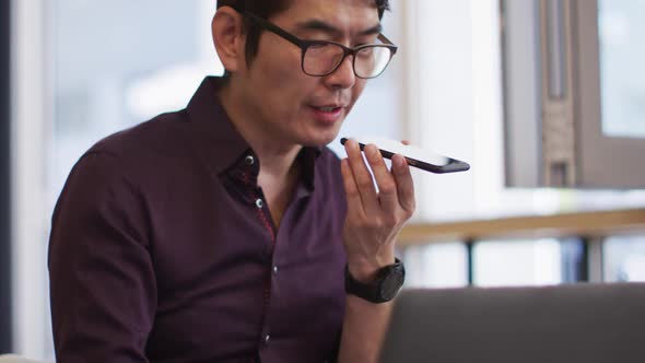 Asian man with laptop talking on smartphone while sitting at a cafe