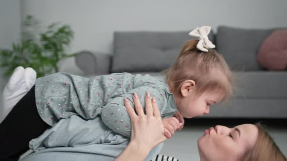 Happy Childhood Smiling Young Mother Kissing Her Female Child Tenderly While Playing Plane in Room