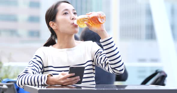 Woman Look at Mobile Phone and Drink of Bottle of Tea